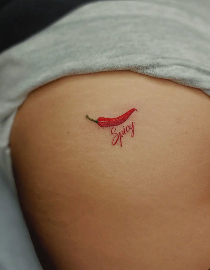Small tramp stamp tattoo of a red chili pepper with the word spicy on the lower back of a person. Small tramp stamp tattoo of a red chili pepper with the word spicy on the lower back of a person.