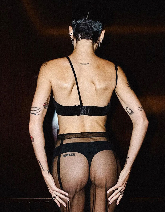 Person wearing black lingerie and sheer stockings showing a tramp stamp tattoo on the upper buttocks in a dark setting. Person wearing black lingerie and sheer stockings showing a tramp stamp tattoo on the upper buttocks in a dark setting.