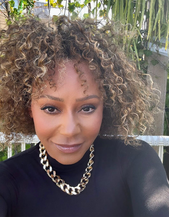 Close-up of a woman with curly hair wearing a black top and gold chain necklace showcasing the tramp stamp tattoo trend. Close-up of a woman with curly hair wearing a black top and gold chain necklace showcasing the tramp stamp tattoo trend.
