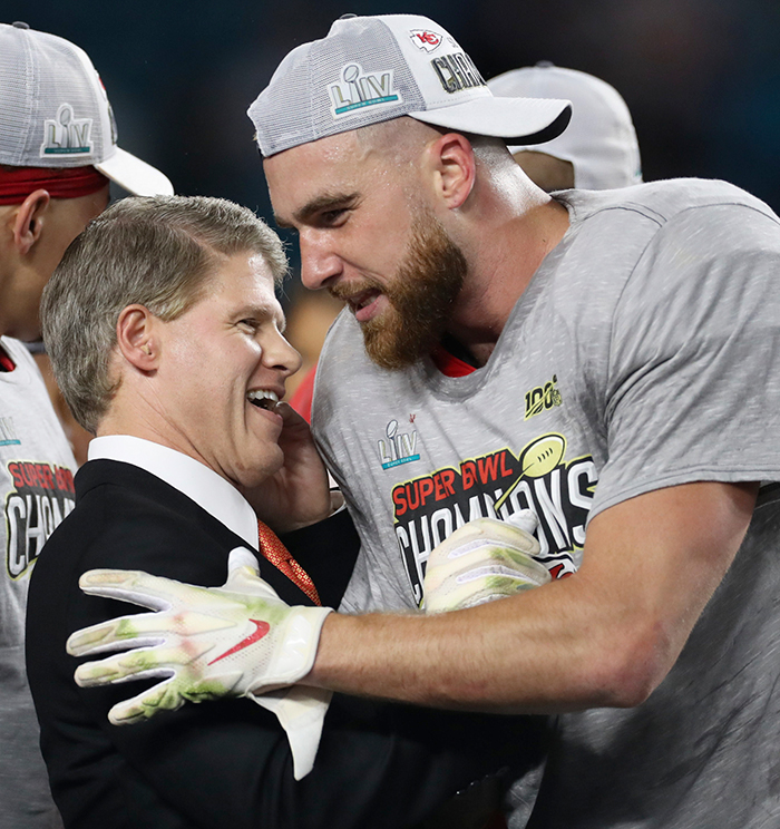 Man in Kansas City Chiefs Super Bowl champions gear embracing a suited man, related to family of Travis Kelce's boss in Texas floods story