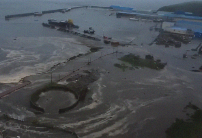 Flooded coastal area with strong tsunami waves hitting the shore after mega earthquake, showing damaged structures and rising waters.