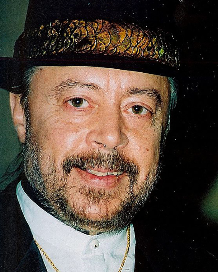 Portrait of a legendary jazz musician wearing a decorated hat and white collar, smiling softly against a dark background. - 7