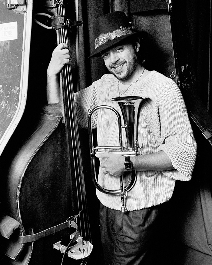 Legendary jazz musician smiling while holding a trumpet and standing next to a double bass in a black and white photo. - 3