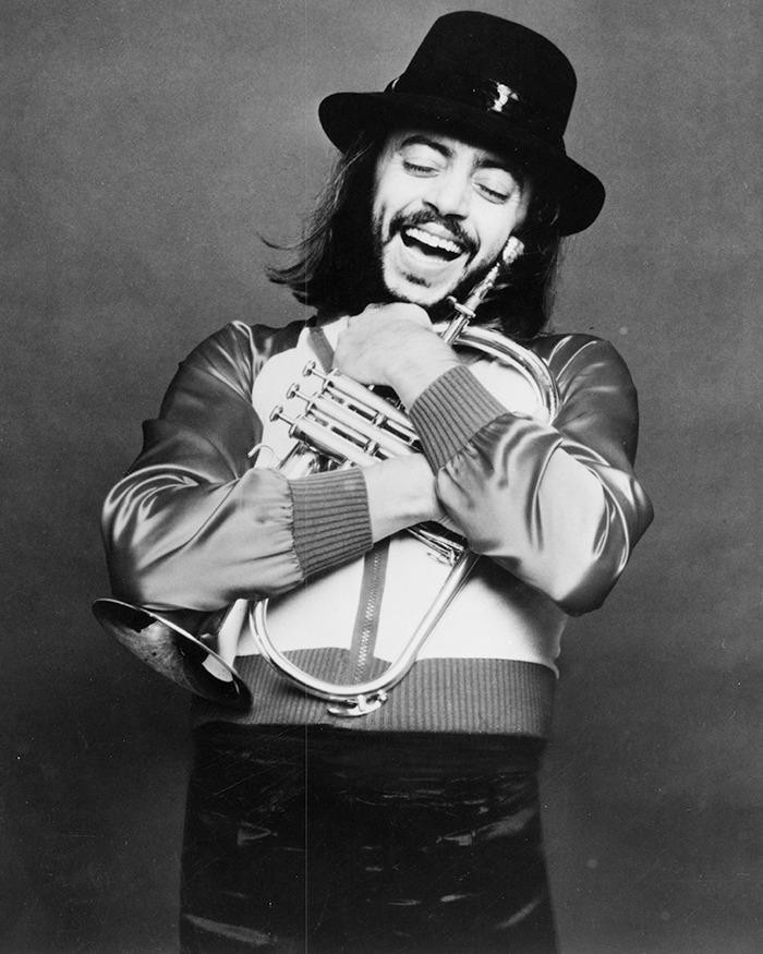 Legendary jazz musician smiling and hugging a trumpet, wearing a hat and satin jacket in a black and white photo. - 2