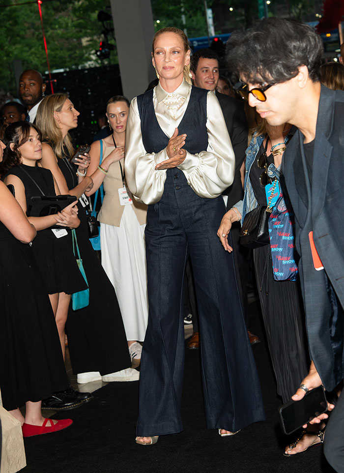 Tall female star wearing a satin blouse and wide-leg pants at a crowded event, showcasing super tall celebrity style.