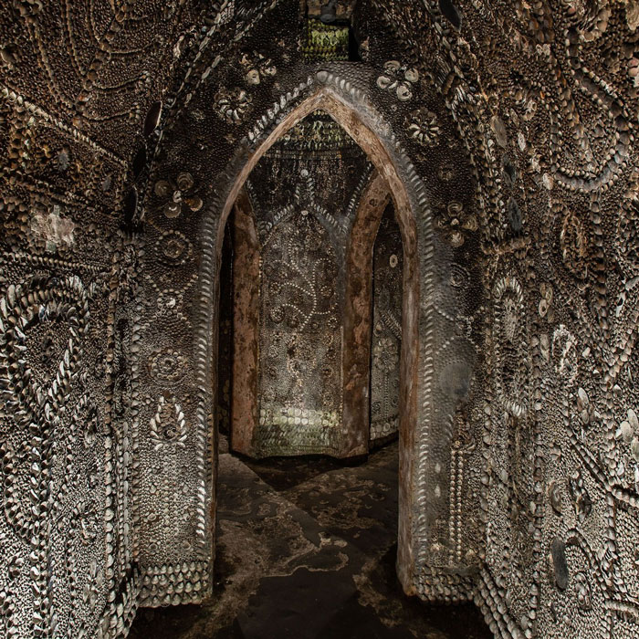 Underground grotto with walls and arches covered in millions of seashells forming intricate patterns and designs.