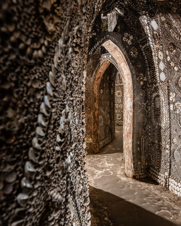 Underground grotto covered in millions of seashells with intricate patterns and arched stone doorways.