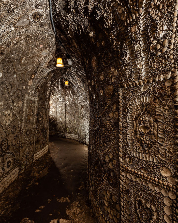Underground grotto interior covered in millions of seashells with intricate patterns and dim hanging lights.