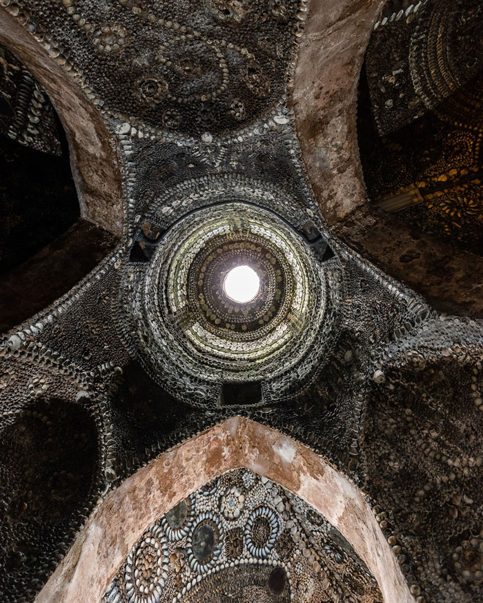Underground grotto ceiling covered in millions of seashells, showcasing intricate patterns around a bright central opening.