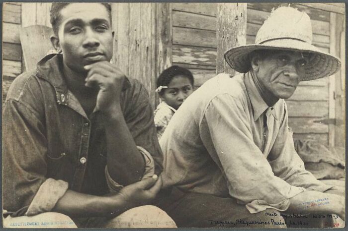 Two men and a child sitting outside a wooden building in a rare photo from the Great Depression era capturing daily life.