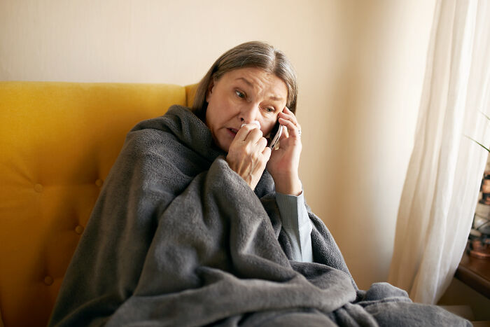 Woman wrapped in blanket looking upset while talking on phone, depicting unhinged family member at wedding situation. - 2
