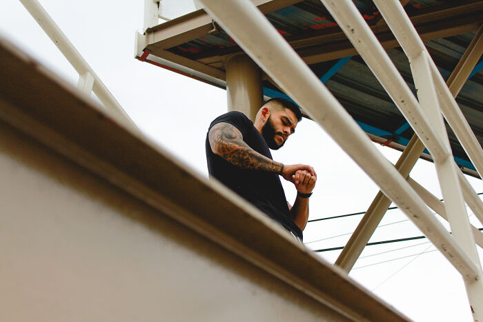 Man with tattoos looking at his watch under metal beams, representing unhinged family member wedding tension. - 11