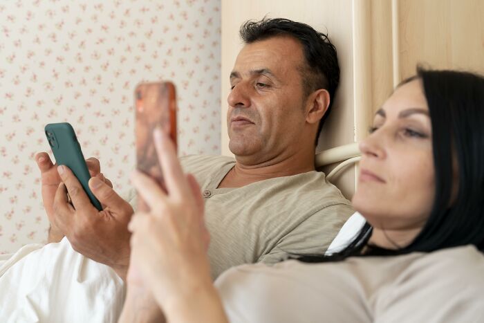 Couple in bed focused on their phones, reflecting a tense moment with an unhinged family member at a wedding. - 33