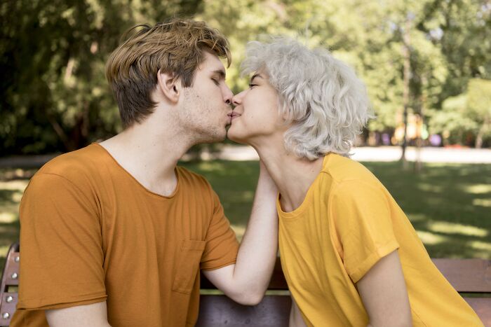 Young couple sharing a kiss on a park bench, representing an unhinged family member wedding scenario outdoors. - 22