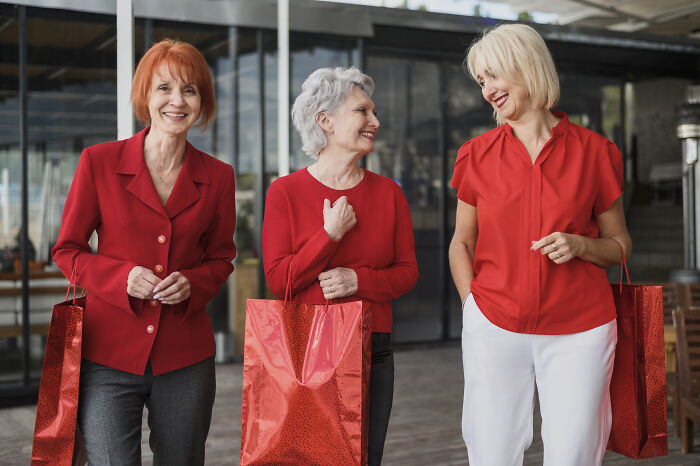 Three women smiling and holding red gift bags, dressed in red, reflecting a lively unhinged family member wedding atmosphere. - 14