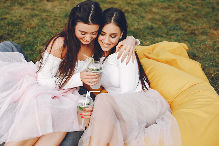 Two young women in tulle skirts sharing drinks and hugging on a beanbag, capturing a calm wedding moment without unhinged family member. - 31