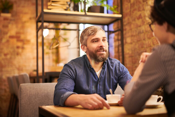 Man with beard and blue shirt talking intensely over coffee, depicting unhinged family member wedding conversation. - 3