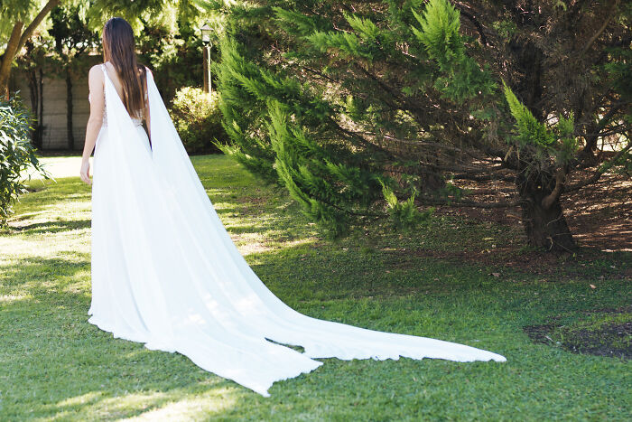 Bride in a long white dress walking on grass near trees, with an unhinged family member wedding atmosphere implied. - 7