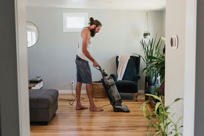 Man using a vacuum cleaner in a living room, demonstrating life hacks that improve daily life quality and efficiency.