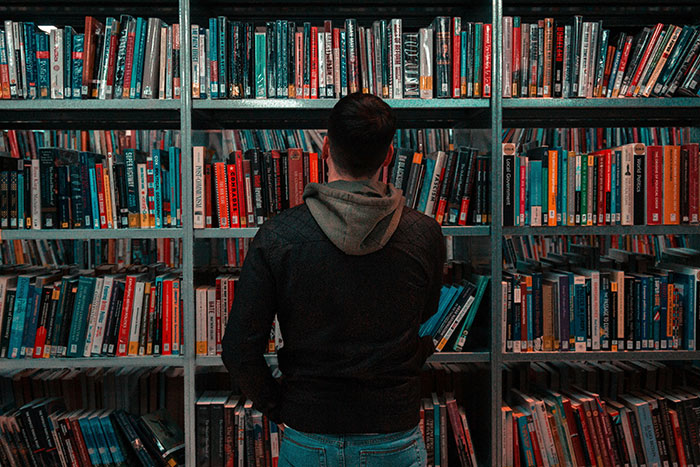 Person standing in front of a full bookshelf, exploring life hacks that actually work and improve life quality.
