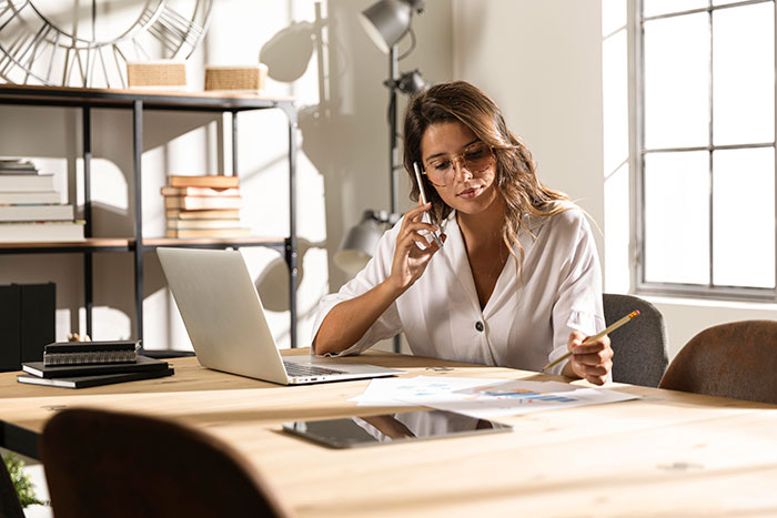 Woman using laptop and phone while working on life hacks that actually work to improve life quality at home office.