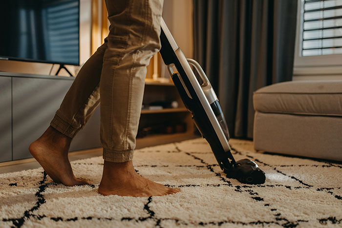 Person using a cordless vacuum cleaner on a carpet, demonstrating life hacks that improve life quality at home.