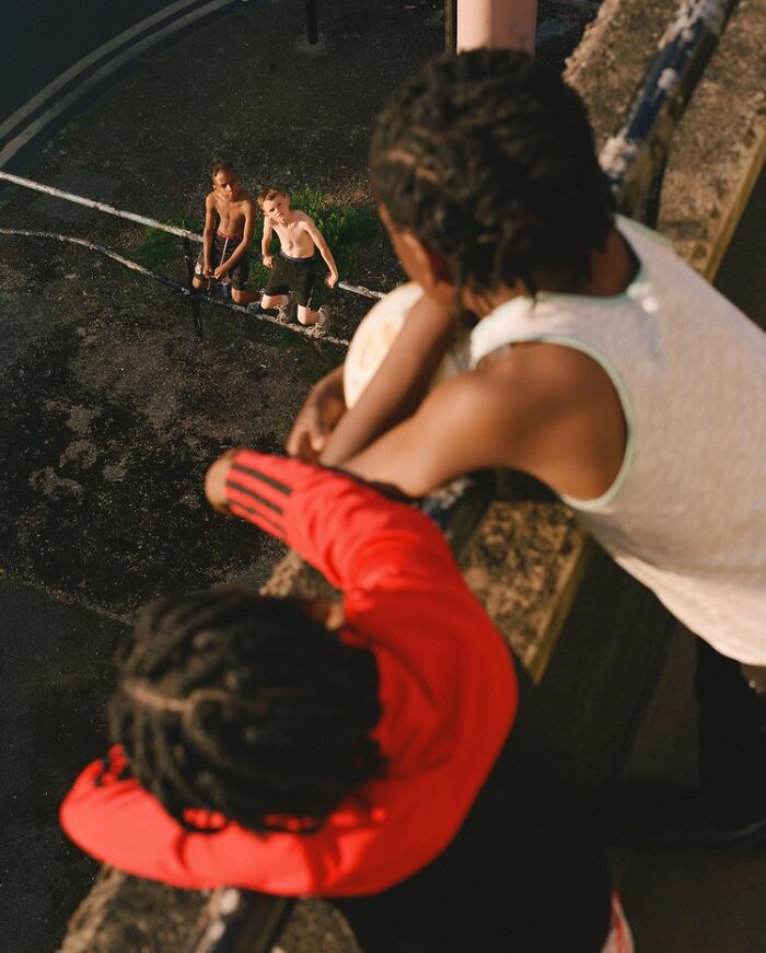 Two boys looking up from a ledge at two shirtless boys playing below on the streets of London.