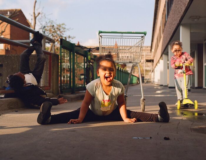 Children playing on a sunny London street with a shopping trolley and scooter, captured in honest photos by Nico Froehlich.