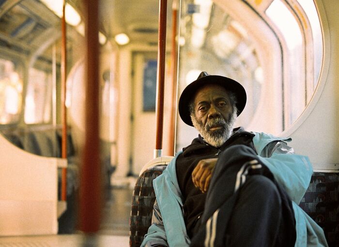 Man wearing a hat and light jacket sitting inside a London Tube train in an honest street photography style by Nico Froehlich.