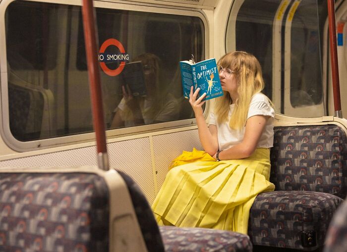 Young woman reading a book on the London Tube, captured in an honest street photo by Nico Froehlich.