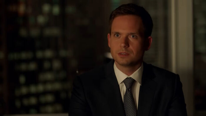 Man in suit and tie sitting indoors at night, representing shows with characters that are hard to love. - 22