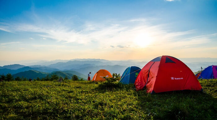 Colorful tents set up on a grassy hilltop with mountains in the background during a vacation destination poll trip.