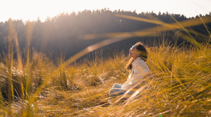 Woman sitting in tall grass at golden hour enjoying nature and peaceful moment at a vacation destination poll site outdoors