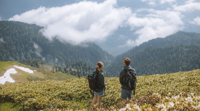 Two hikers with backpacks overlooking a mountain range and cloudy sky in a vacation destination poll setting.