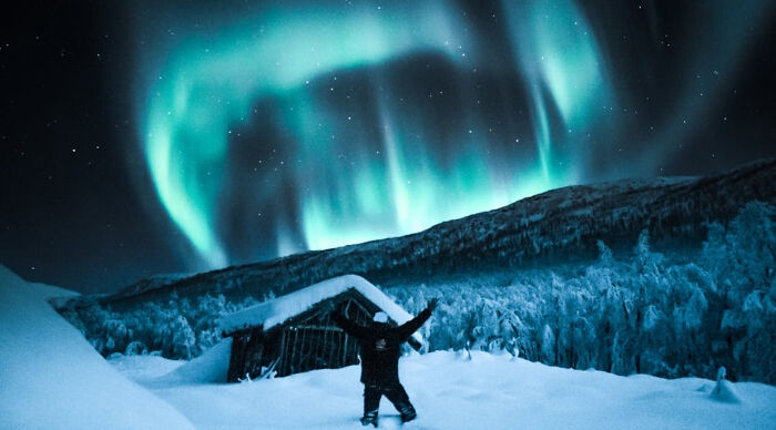 Person standing in snowy landscape under vibrant northern lights in a scenic vacation destination poll setting.