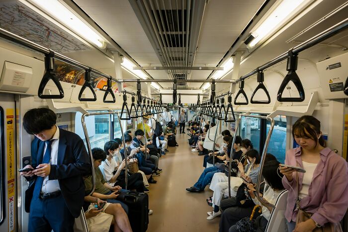 Passengers on a crowded train engrossed in their phones, illustrating unusual public behavior in urban settings.