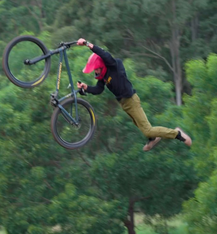 21-year-old daredevil mid-air, losing grip of bike during a record-breaking dive attempt in a forested area.