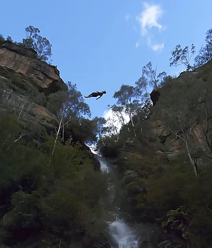 21-year-old daredevil mid-air during a record-breaking dive off cliff surrounded by trees and waterfall below.