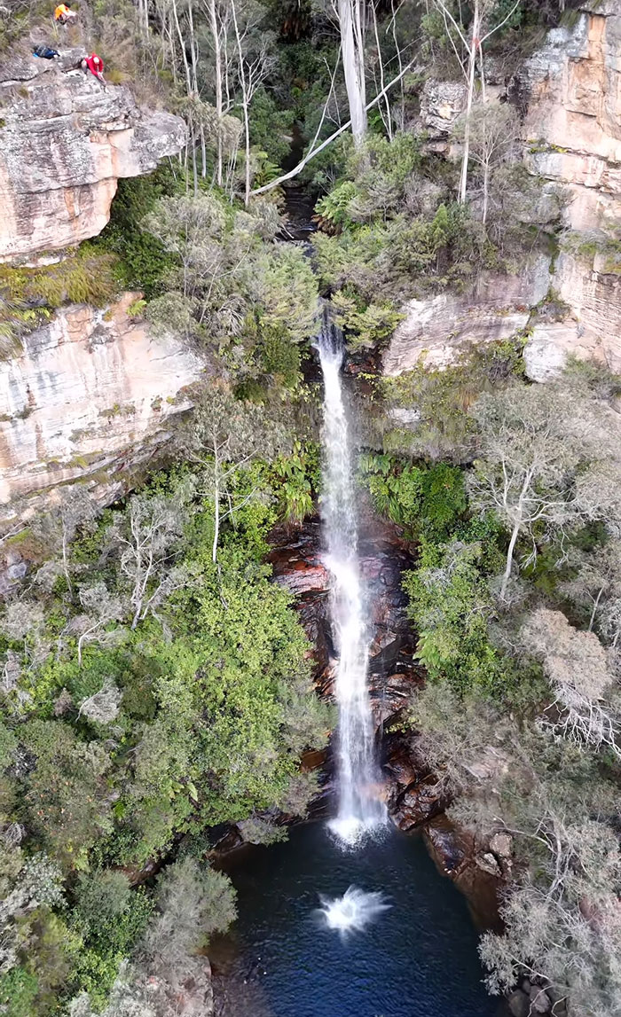 Aerial view of a waterfall with a splash in the pool below as a 21YO daredevil attempts a record-breaking dive.