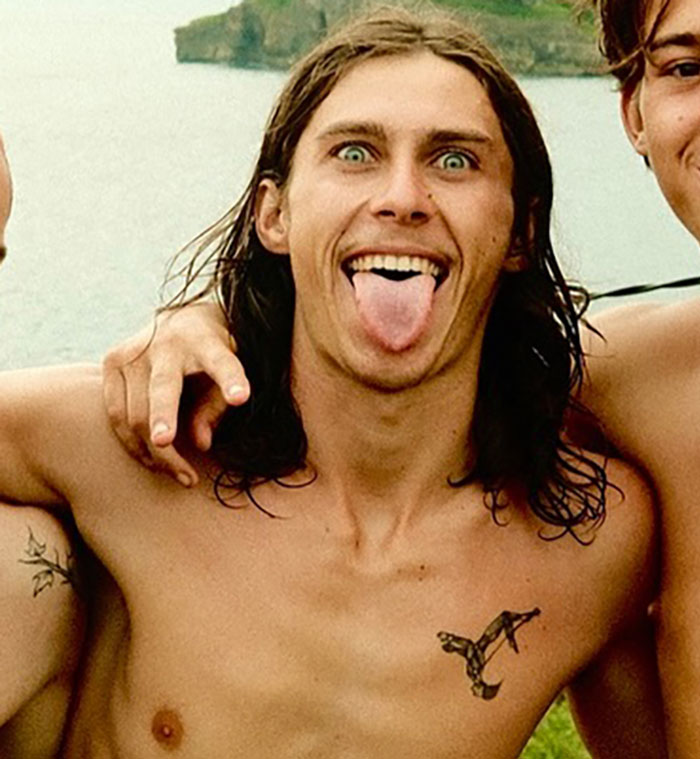 Young daredevil shirtless with long hair sticking out tongue, possibly before attempting record-breaking dive stunt.