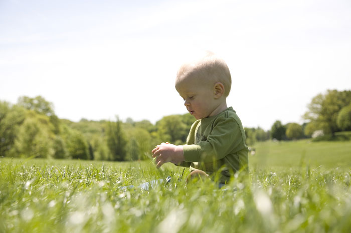 Baby boy sitting in a green field on a sunny day, representing very rare boy names for stand-out babies.