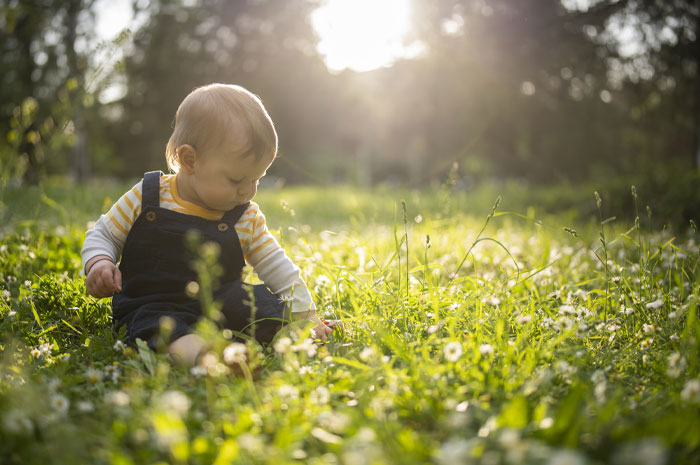 Baby boy sitting in sunlit field of flowers, representing very rare boy names for stand-out babies concept.