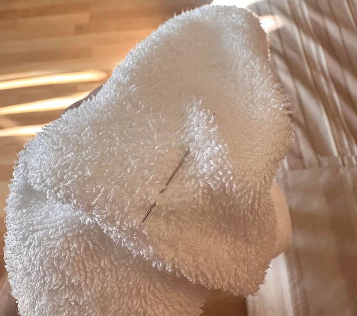 White hotel towel with a sewing needle accidentally left inside, showcasing a hotel mess-up caught by a guest online.