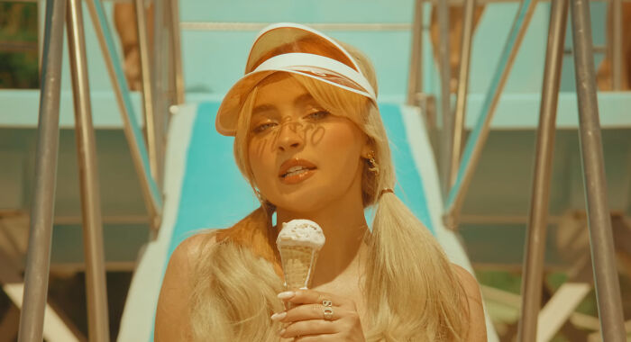 Young woman with blonde hair and visor holding ice cream cone by pool, illustrating celebrities people honestly can't stand.