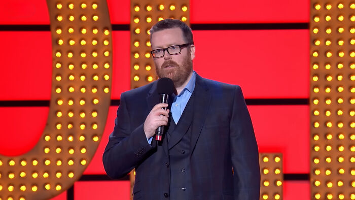 Comedian performing on stage with microphone, discussing unpopular opinions about celebrities many people love.