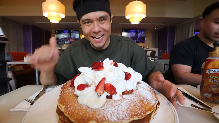 Man sharing large pancakes with whipped cream and strawberries, representing people share unsubscribed YouTubers content.
