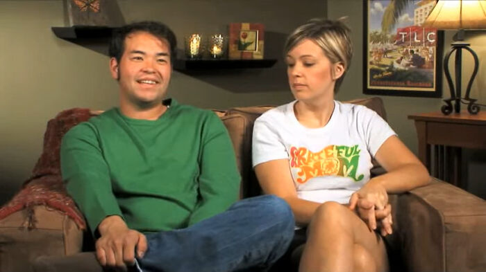 Two people sitting on a couch discussing outrageous student names revealed by a teacher in a casual home setting.