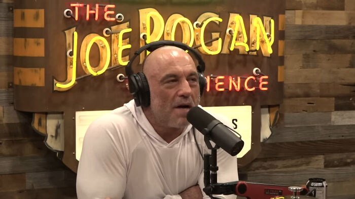Joe Rogan podcast host wearing headphones and speaking into a microphone about people who share unsubscribed YouTubers.