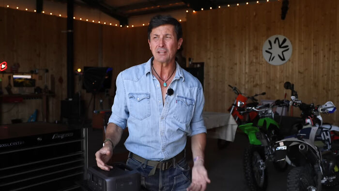 Man in casual denim shirt sharing thoughts about people who share unsubscribed YouTubers in a garage with motorcycles.