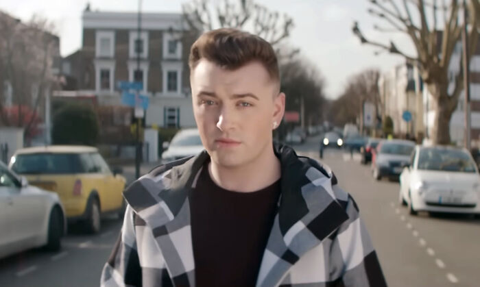 Young man standing on a city street, wearing a checkered jacket, representing celebrities many people love but can't stand.
